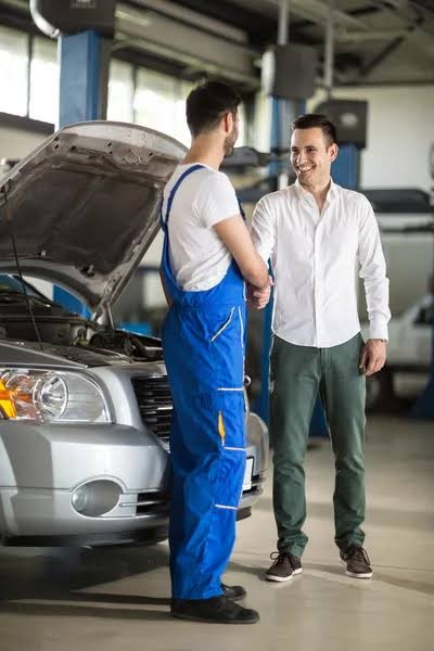 Mechanic shaking hands with a happy customer next to their car